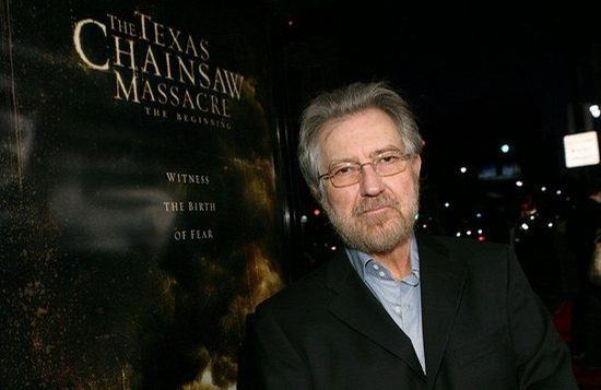 Tobe Hooper, criador da franquia ao lado do cartaz de "Massacre da Serra Elétrica: O início"